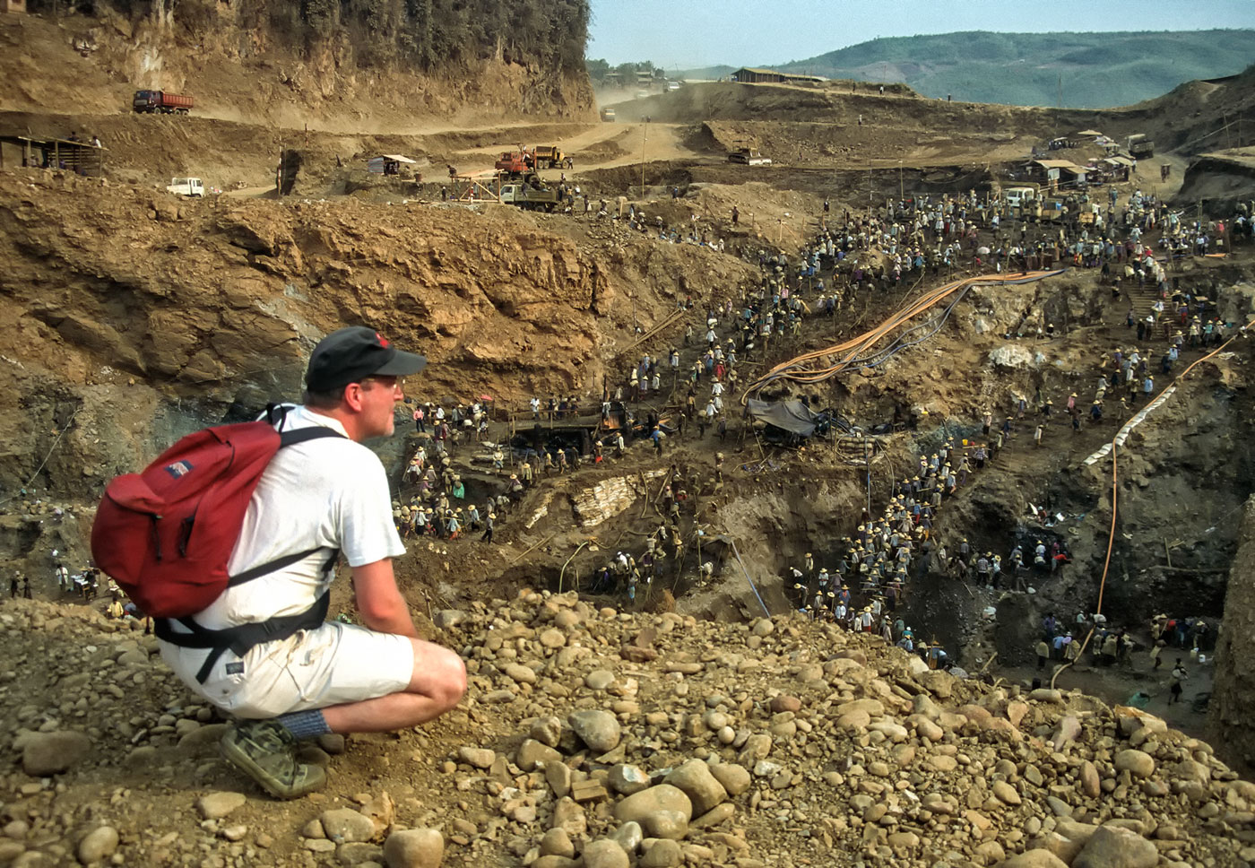 Figure 12. Thousands of workers remove the dirt and gravel at Hpakangyi to reach the Uru conglomerate and its promise of fine jadeite. Using the most rudimentary of carrying devices – two crudely fashioned bamboo buckets – this young miner leads a trail of laborers up the steep path from the bottom of the pit to a truck that will carry the waste to the river. Photo © Richard W. Hughes. Click on the image for a larger photo.